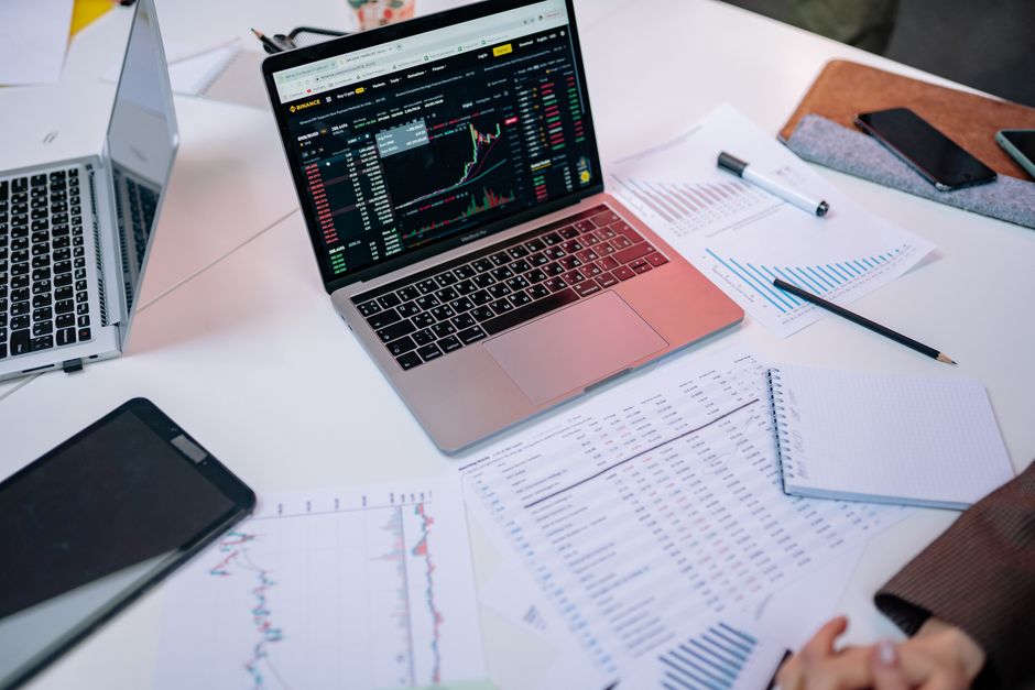 Economia do Turismo — Laptops on a desk displaying stock market charts and financial documents.