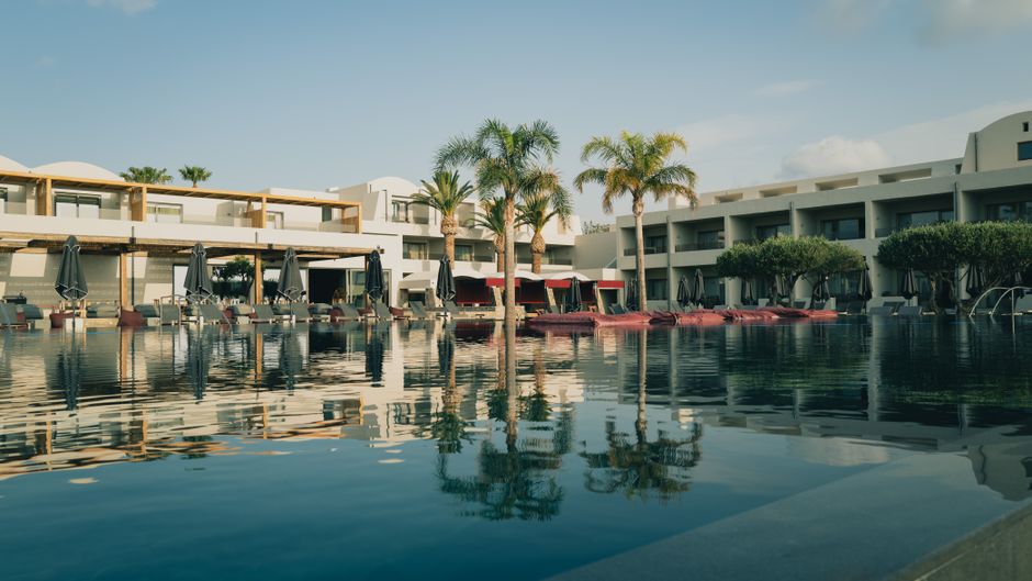 Economia do Turismo — Elegant resort with a pool and palm trees under a clear blue sky in Greece.