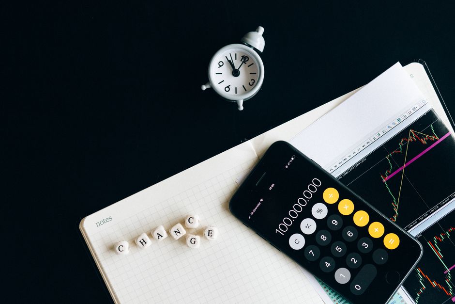 Economia do Turismo — Notebook with an iPhone displaying 100,000,000, desk clock and financial charts suggesting market