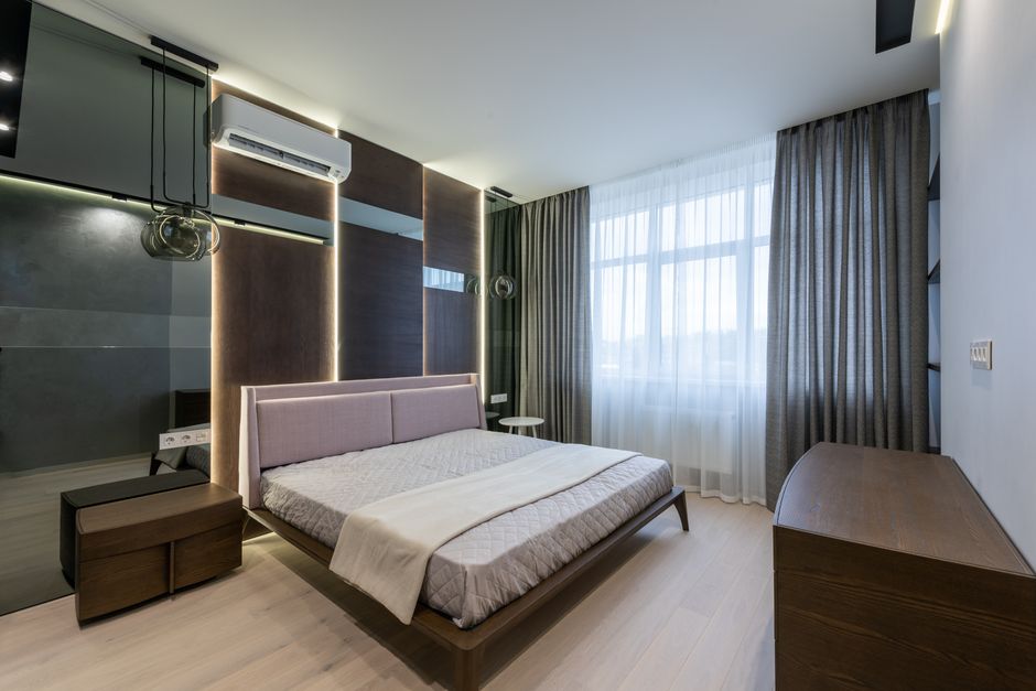 Economia do Turismo — Comfortable bed with wooden nightstand and chest of drawers in modern bedroom decorated with curtains