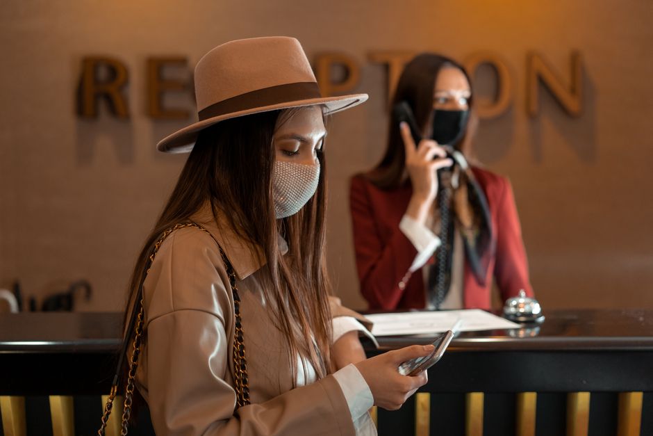 Economia do Turismo — Woman wearing a mask checking her phone at a hotel reception during COVID-19.