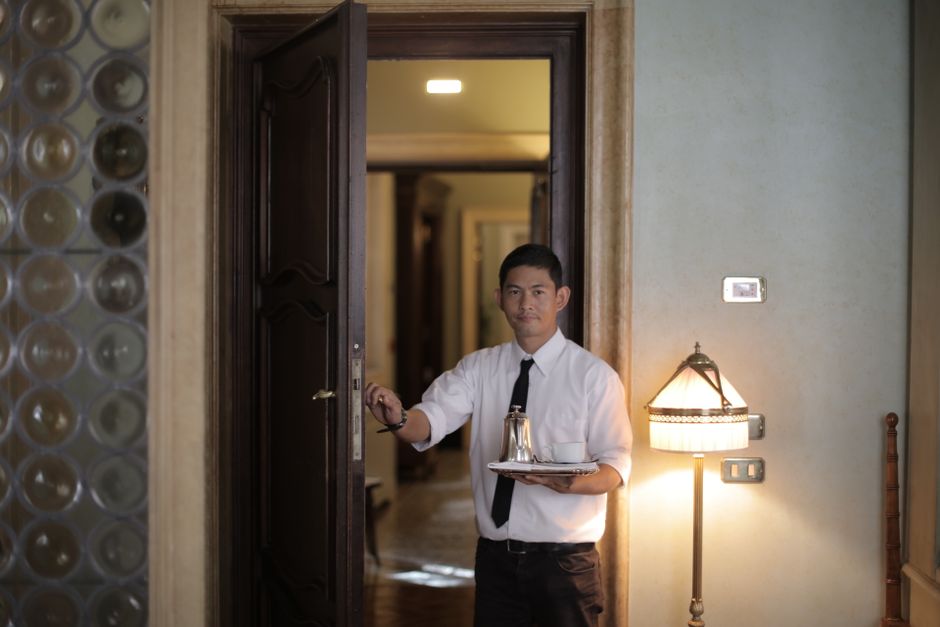 Economia do Turismo — Friendly ethnic male waiter serving clients in room and carrying tray with coffee while working in